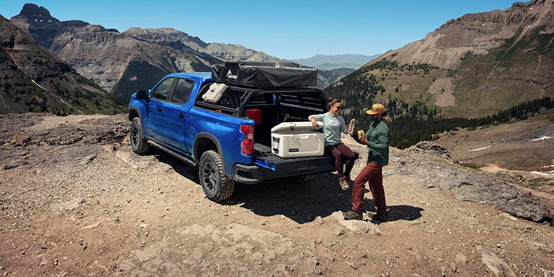 A Coupe sat in the back of a 2025 Chevrolet Silverado 1500 on a dirt trail.