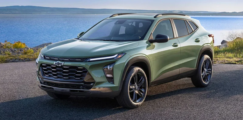 A green 2026 Chevy Trax parked on a gravel parking lot near a lake.